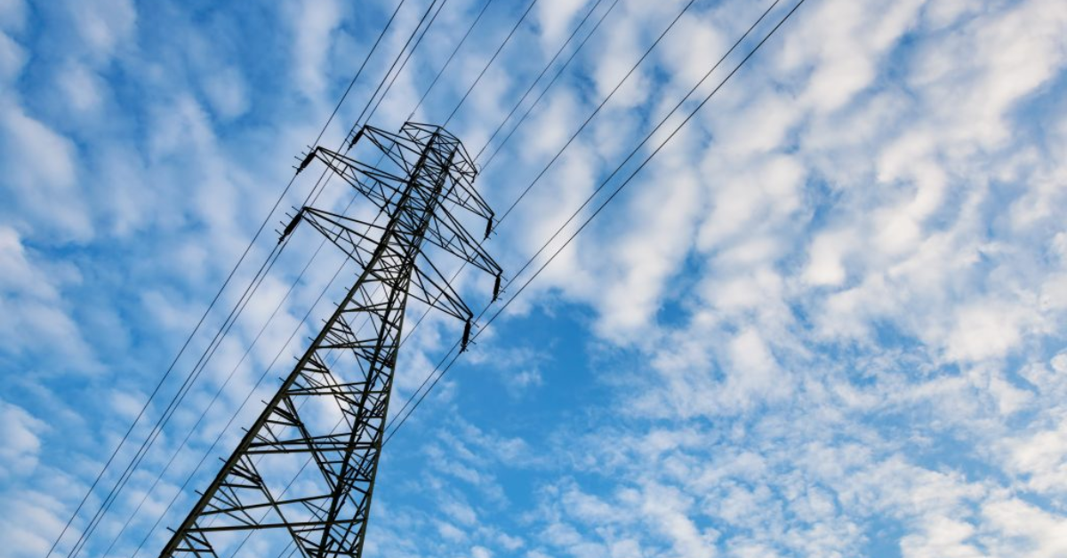 Electricity transmission pylon against blue sky with fluffy clouds